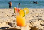 exotic cocktail in sand with sea behind it