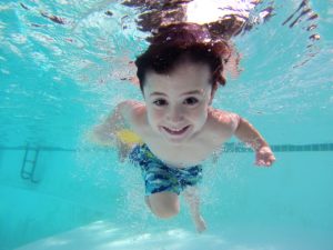 boy in blue swimming trunks looking under water