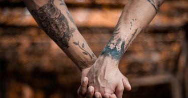 Two persons wearing tattoos on the arms and holding hands.
