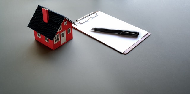 Casa en miniatura junto con papel y boli.
