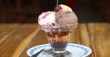 glace composée de trois boules de cerise sur une assiette blanche sur table en bois