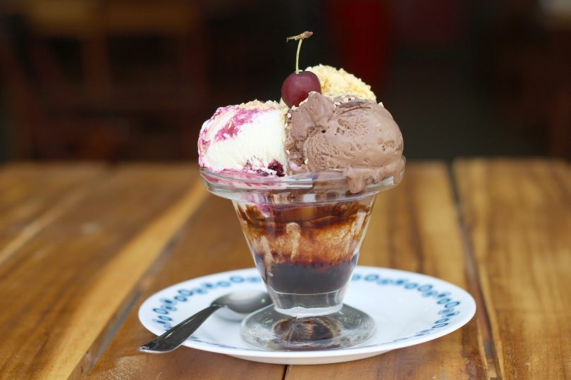 glace composée de trois boules de cerise sur une assiette blanche sur table en bois