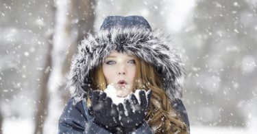 femme avec un manteau d'hiver soufflant sous la neige