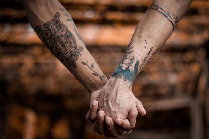 Deux personnes se tenant la main, et ayant les bras tatoués.