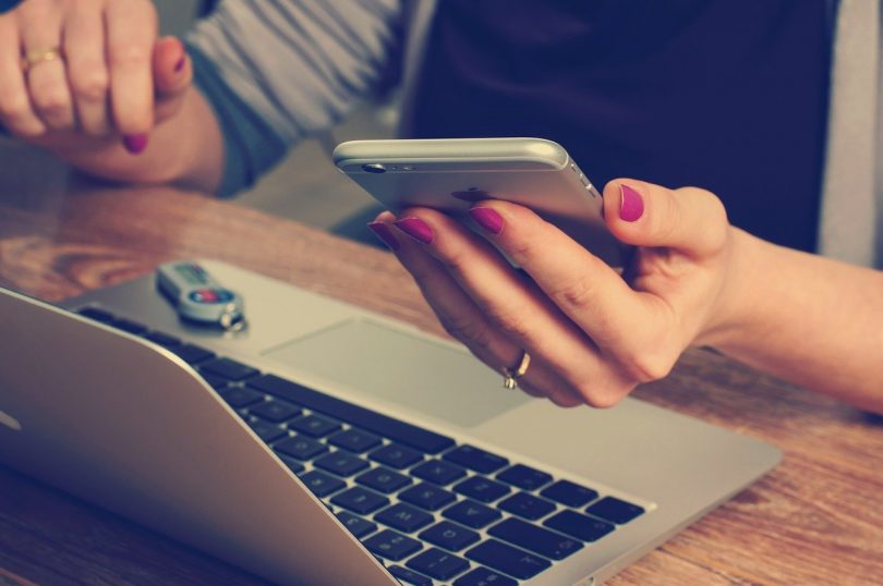 main de femme tenant un mobile devant un ordinateur