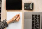 femme écrivant sur un bureau avec une calculatrice et un laptop
