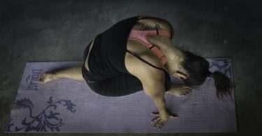 lady in dark environment in yoga pose on purple yoga mat