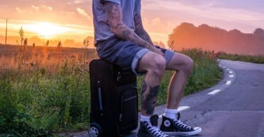 man with tattoo sitting on suitcase