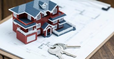 miniature house on building plans with keys