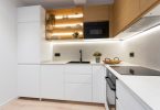 Cocina reformada con muebles blancos y color madera y unas luces de led en las estanterías.