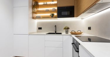 Cocina reformada con muebles blancos y color madera y unas luces de led en las estanterías.