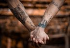 Deux personnes se tenant la main, et ayant les bras tatoués.