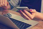 main de femme tenant un mobile devant un ordinateur
