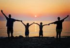 famille les bras levés devant la mer au coucher du soleil
